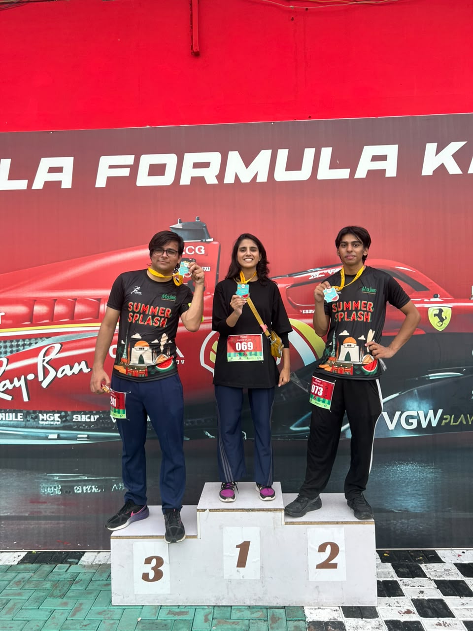 Three runners in Summer Splash shirts posing on a karting podium with medals.