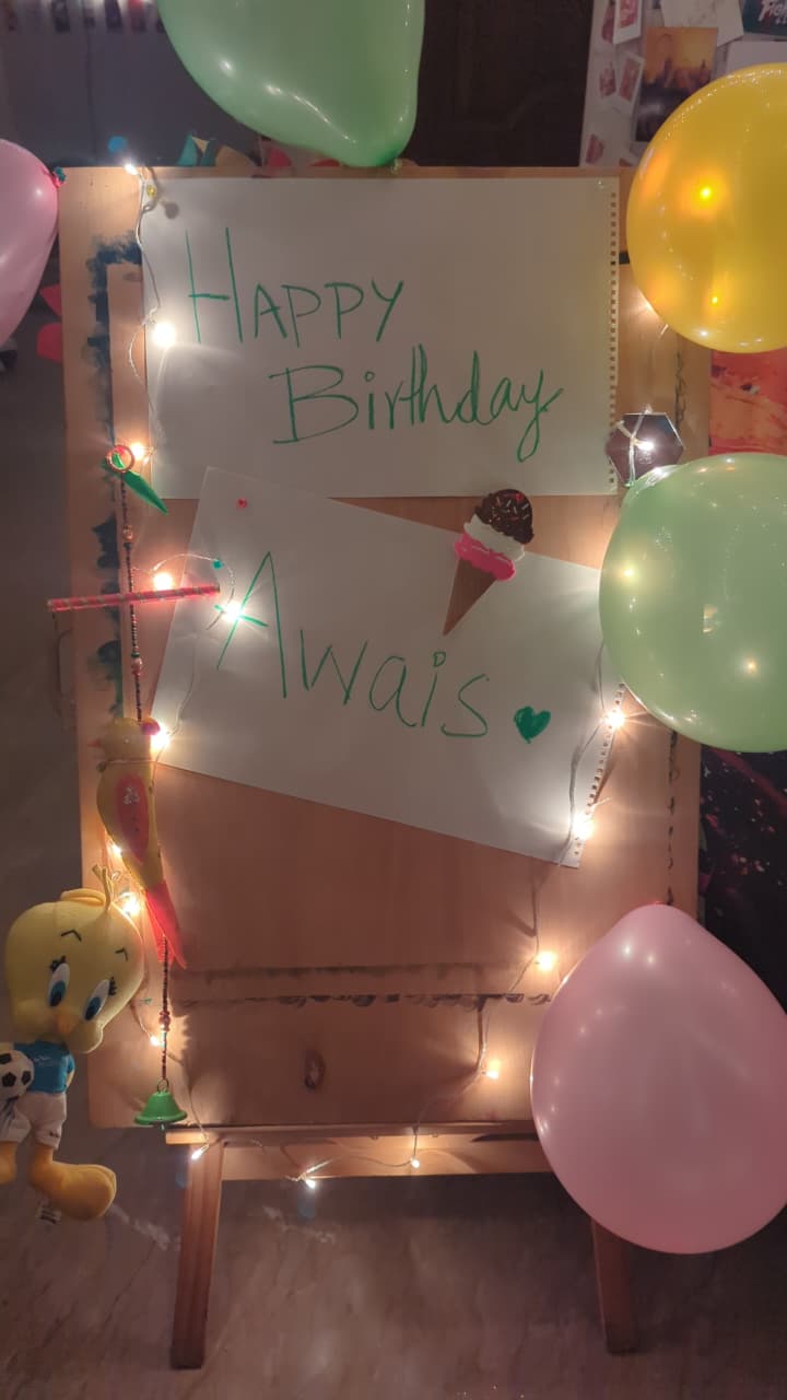 The hand-lettered sign on an easel reading Happy Birthday Awais in green marker, surrounded by balloons and fairy lights.